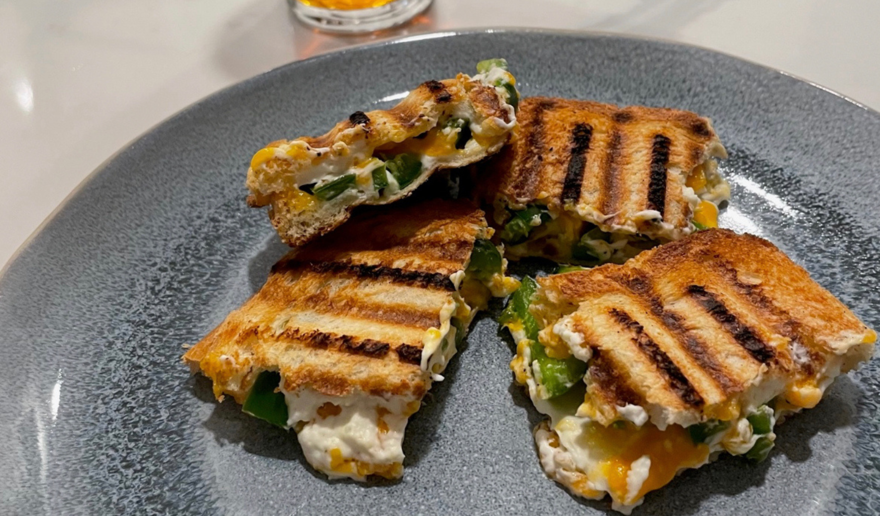 Grilled jalapeño popper sandwich cut in half, cheese melting out, served with a glass of beer for game day.