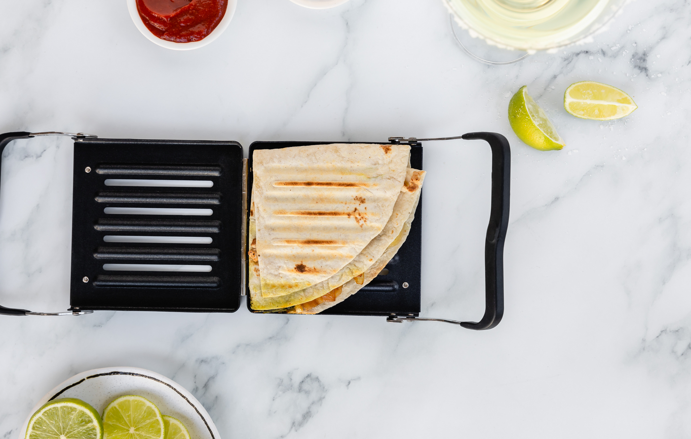 Revolution Toastie Press open on the counter with a toasted Triangle fold quesadilla inside. limes and salsa next to it