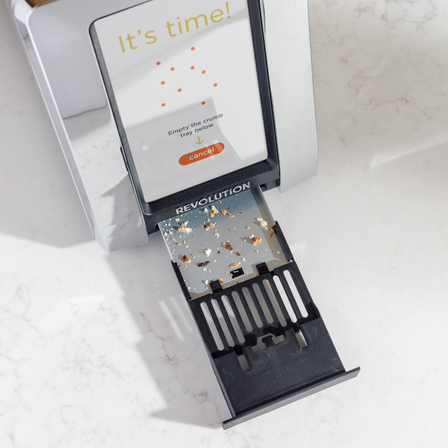 From above, see the Renewed R180 Smart Toaster by Revolution Cooking on a white counter, crumb tray extended with breadcrumbs. The display reads "It's time!" with options to empty the tray. Featuring InstaGLO heating, this toaster blends style and function.
