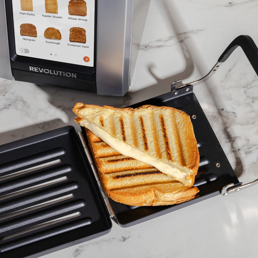 A sandwich in progress on a marble surface features a slice of toast topped with onion jam and another with cheese, accompanied by small bowls of onion jam and sauce. Slices of Swiss cheese are on a wooden board.