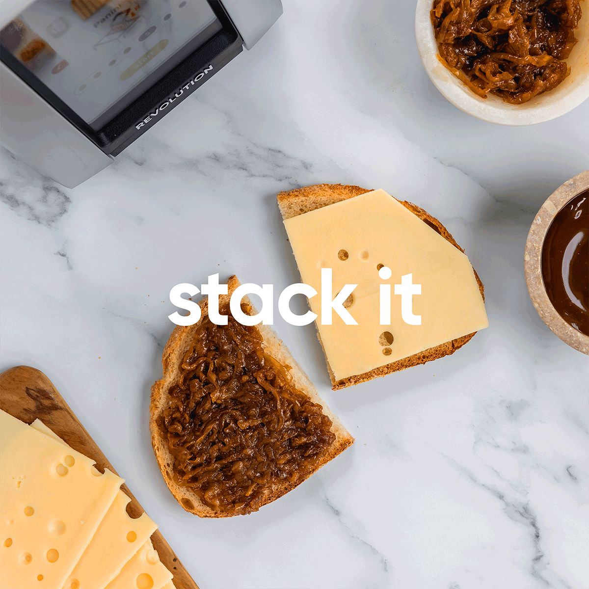 A sandwich in progress on a marble surface features a slice of toast topped with onion jam and another with cheese, accompanied by small bowls of onion jam and sauce. Slices of Swiss cheese are on a wooden board.
