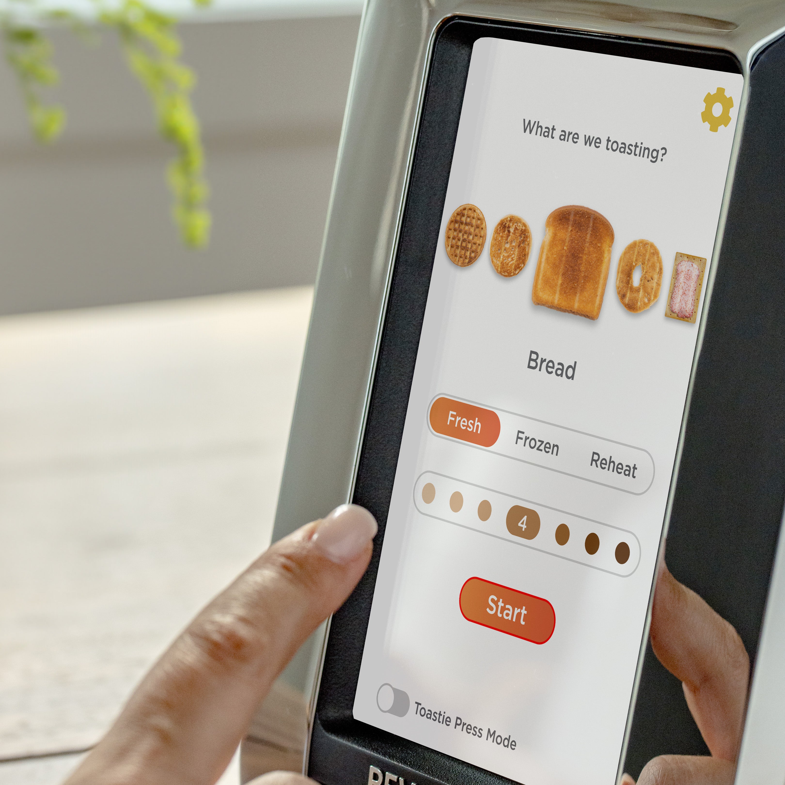 Close-up of someone using the Revolution Cooking R180 Connect Smart Toaster's touchscreen, showcasing InstaGLO® Heating Technology. The display shows options for fresh, frozen, reheat settings, and a doneness scale as a hand effortlessly presses "Start.