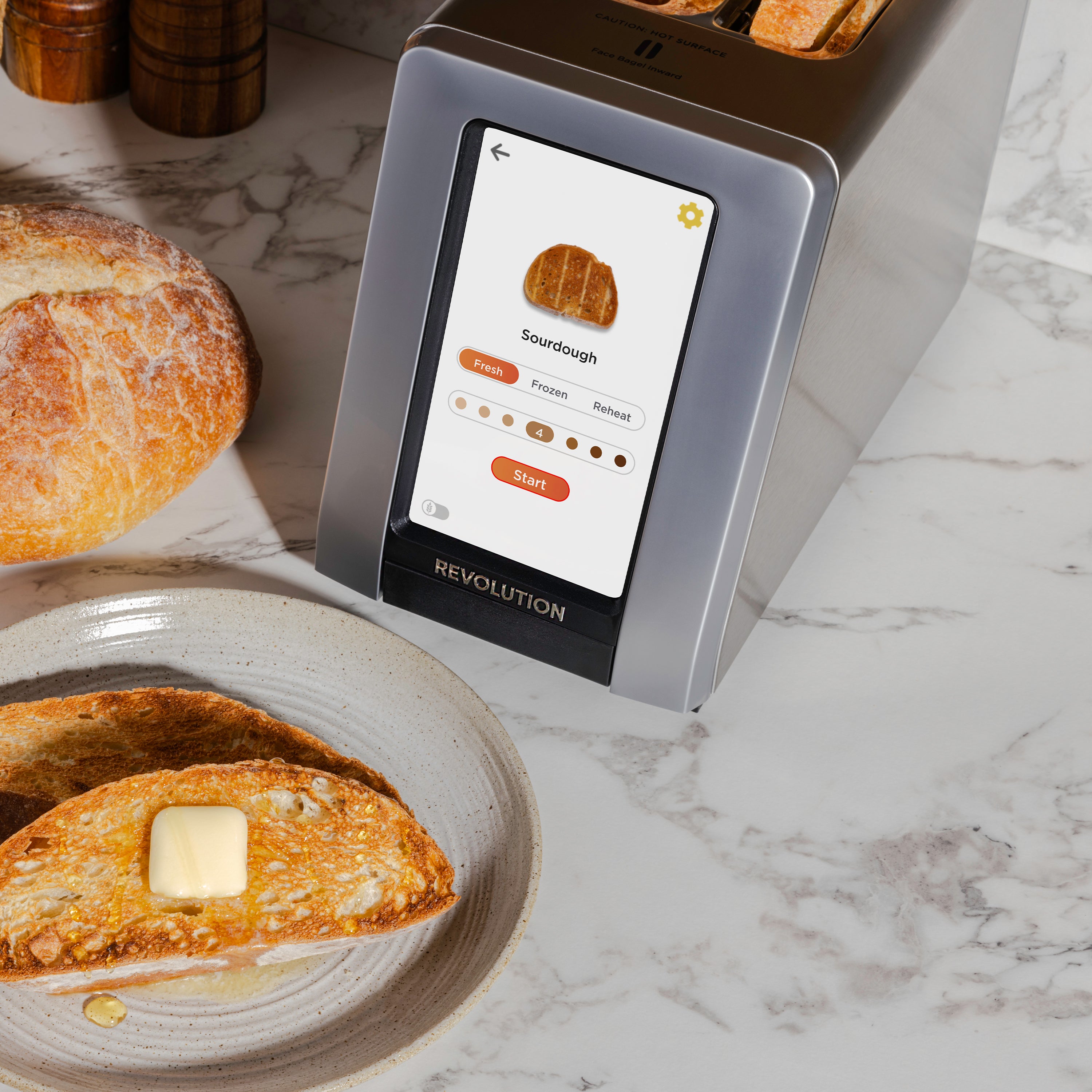 The Revolution Cooking R180 Connect Plus Smart Toaster, equipped with InstaGLO 2.0 technology, features a touchscreen that provides precise toasting options for sourdough bread. Freshly toasted slices topped with butter are neatly arranged on a plate beside an uncut loaf on the marble countertop.