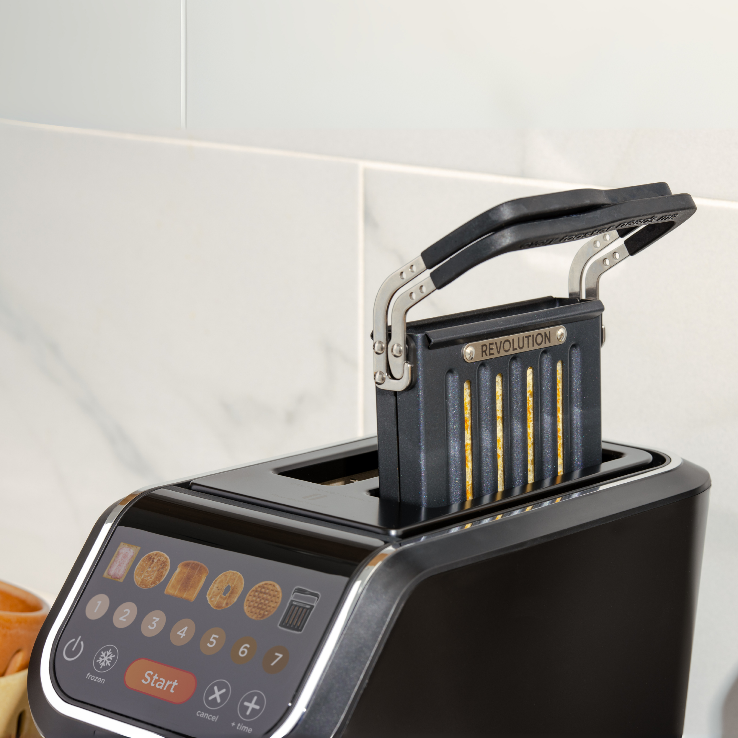 The Revolution Cooking R90 Digital Toaster + Toastie Press in black features a touchscreen and lever, uses InstaGLO technology to toast bread, and is shown against a light-tiled kitchen wall.