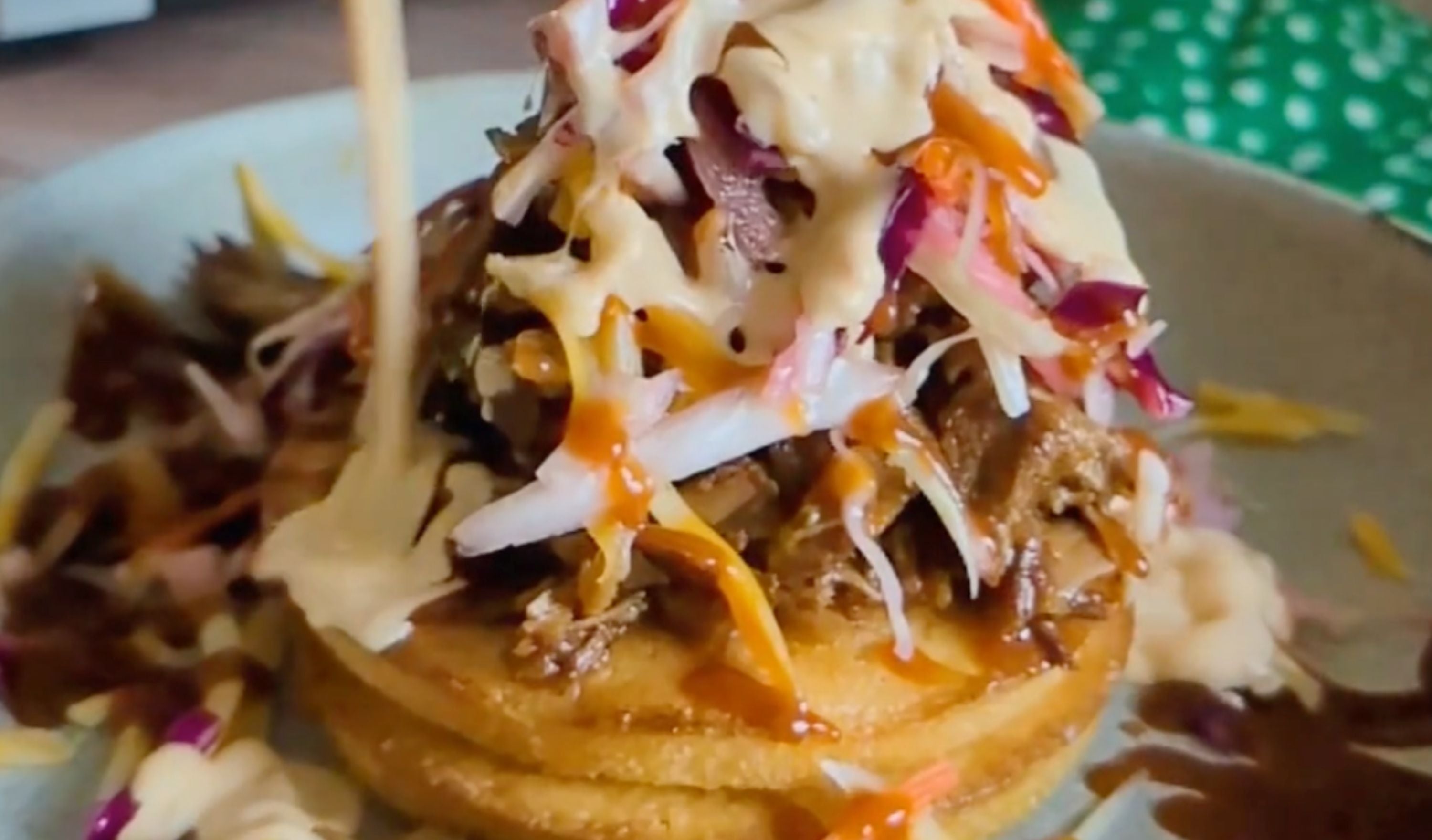 Pulled Pork Sundae stacked on toasted corn cakes with melted cheese, coleslaw, pickled onions, and BBQ sauce.