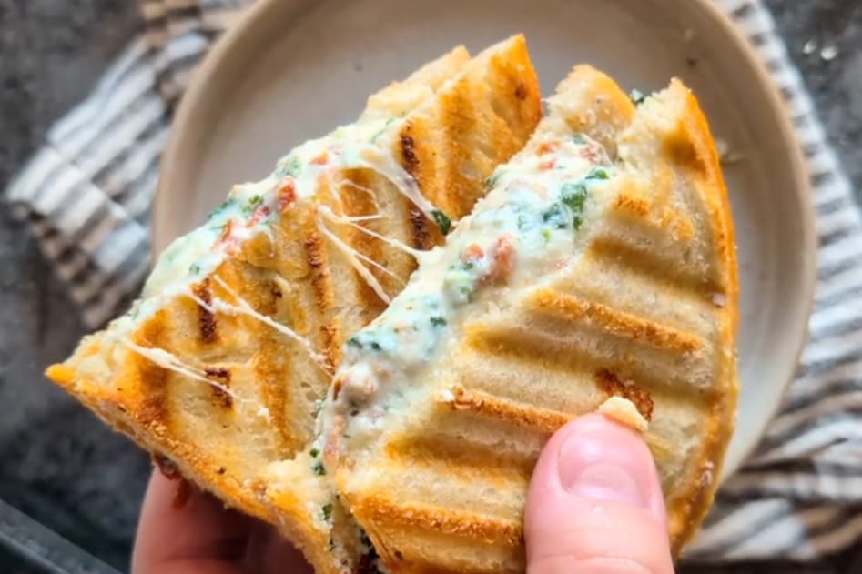 Sun-dried tomato ricotta grilled cheese on sourdough with melted mozzarella and spinach, served on a white plate