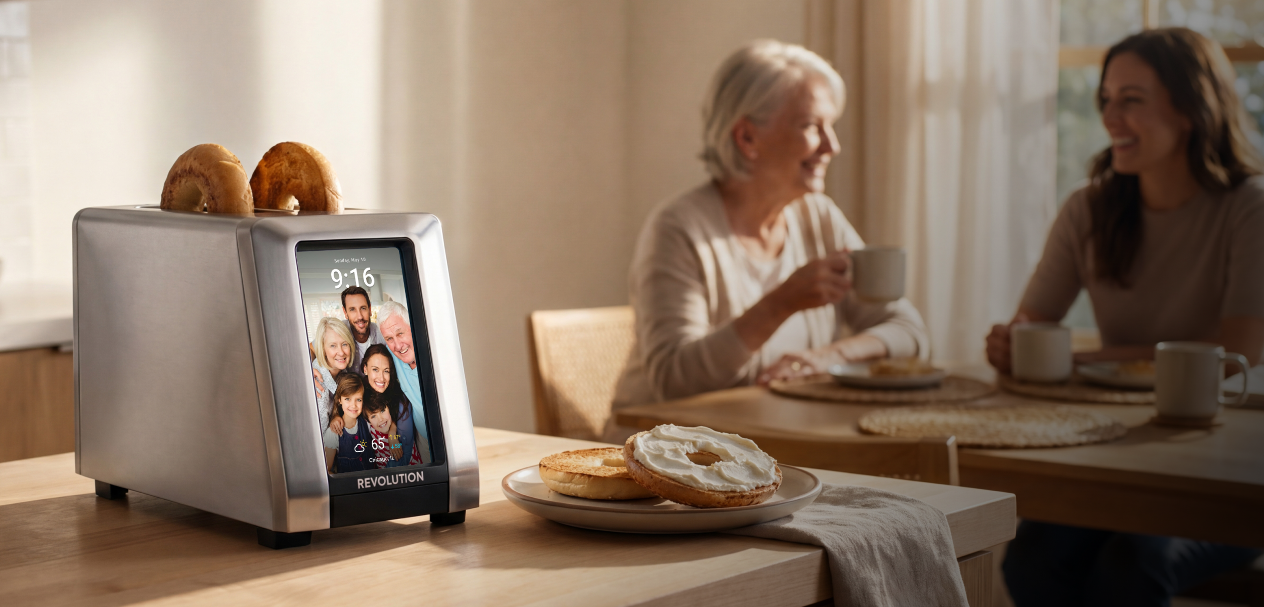 A modern stainless steel smart toaster displaying a family photo on its screen sits on a kitchen counter with toasted bagels, while a mother and daughter share a warm breakfast moment in the background.