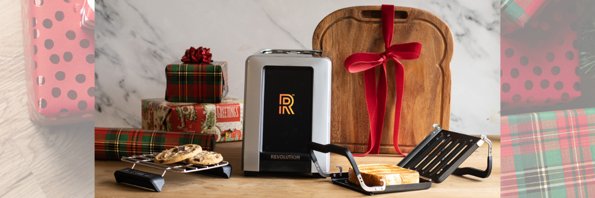 Revolution cooking toaster on a wooden counter with holiday decor around it, and cookies warming on the warming rack above.