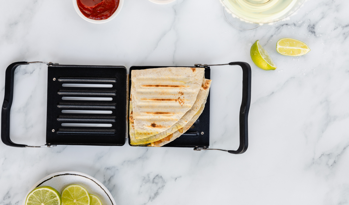 Revolution Toastie Press open on the counter with a toasted Triangle fold quesadilla inside. limes and salsa next to it