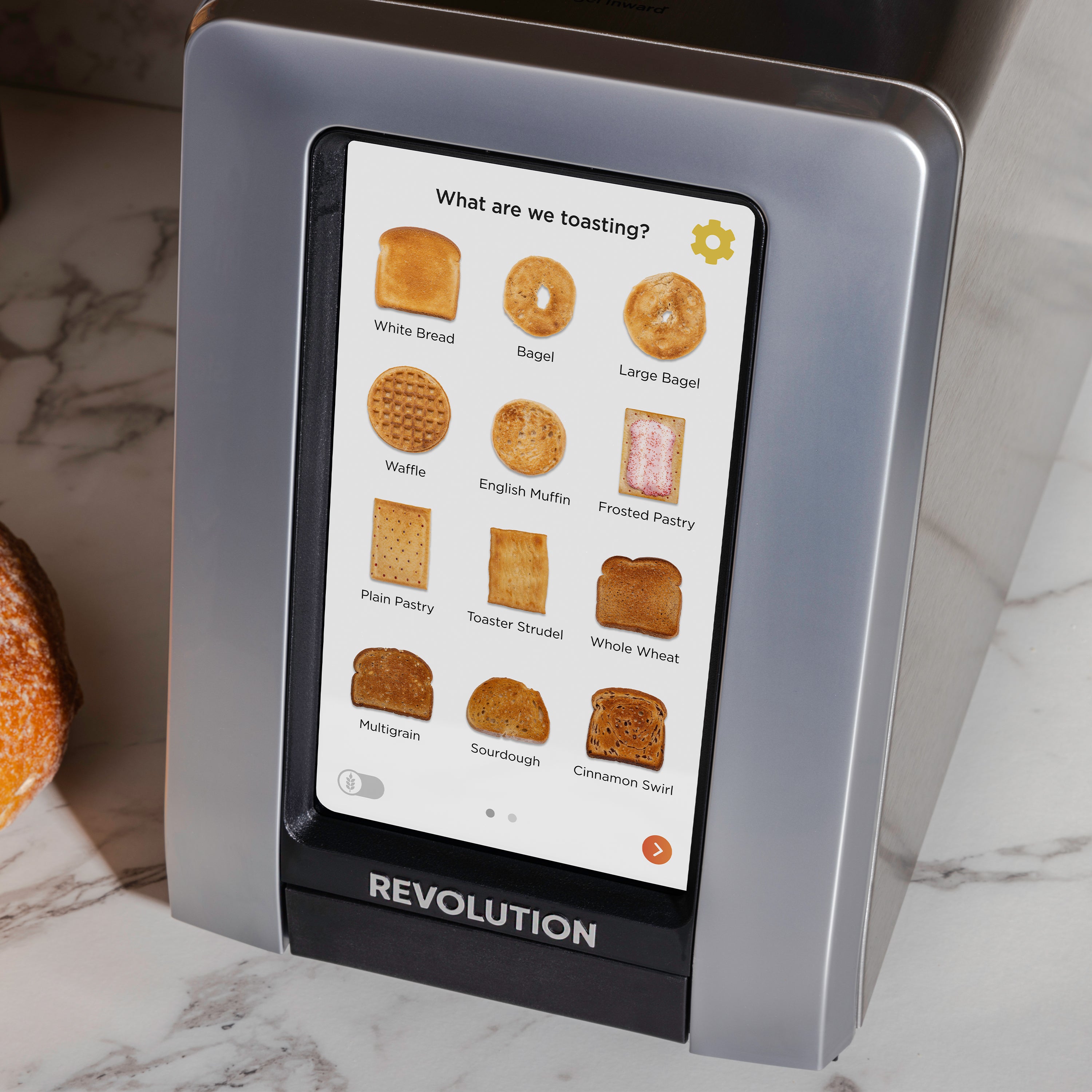 The Revolution Cooking R180 Connect Plus Smart Toaster features a digital display that offers customized toasting options for different types of bread, like white bread, bagels, waffles, and pastries. The sleek interface of this smart toaster stylishly complements a marble countertop.