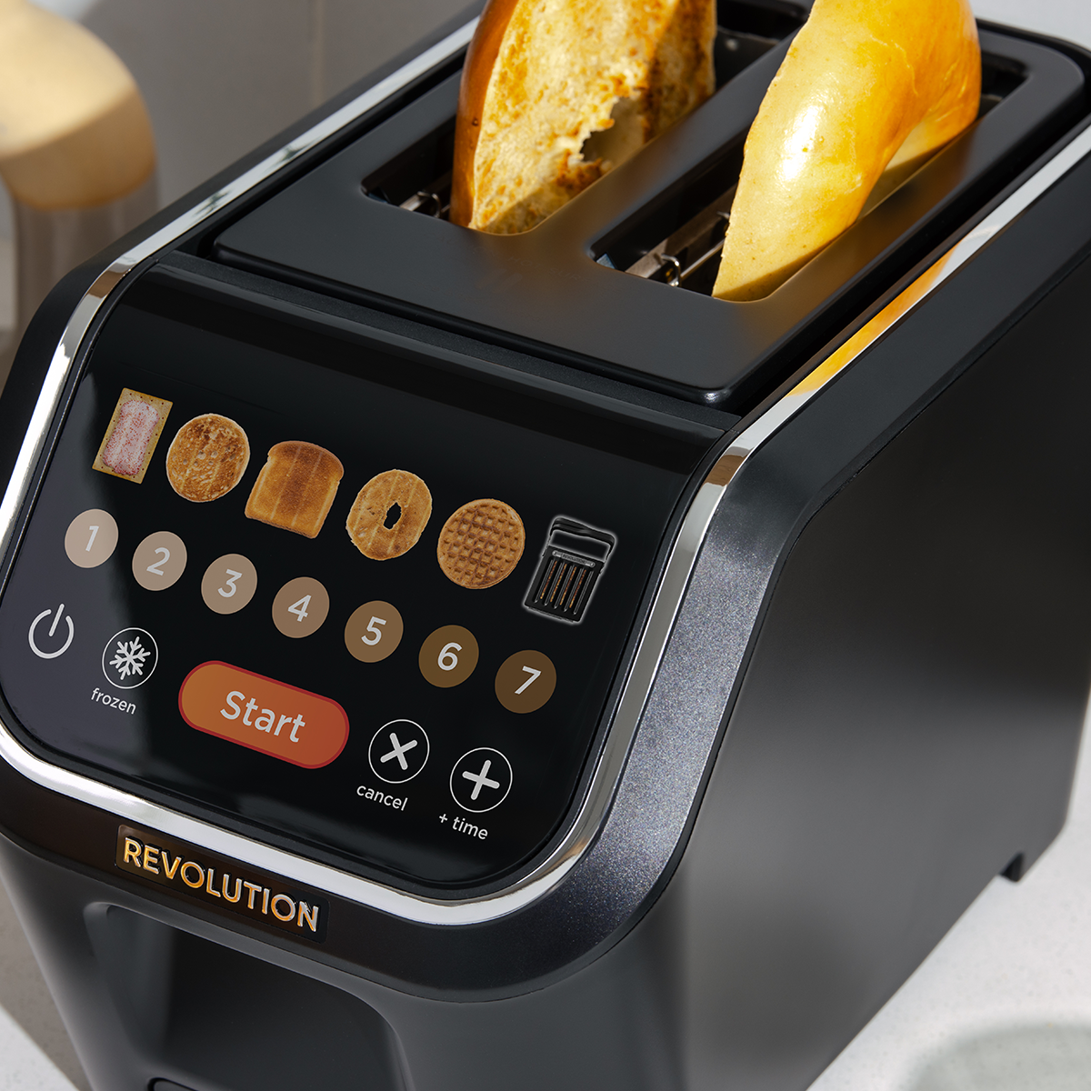 A black Revolution toaster with a digital touchscreen interface displaying various bread options. Two slices of bread are partially toasted in the slots. The toaster features buttons for start, cancel, and time adjustment.